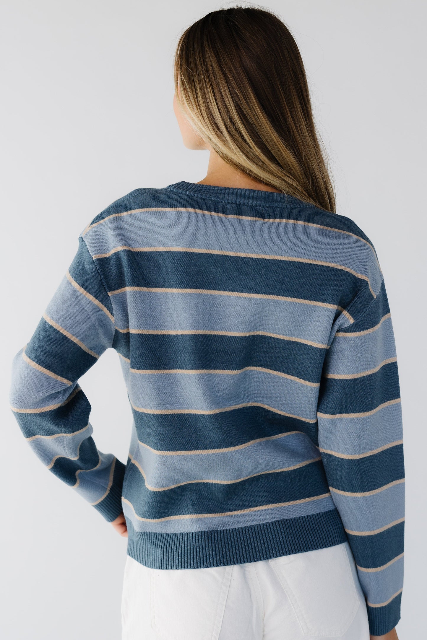 Back view of a woman wearing a blue and darker blue stripe crew neck sweater with long sleeves.