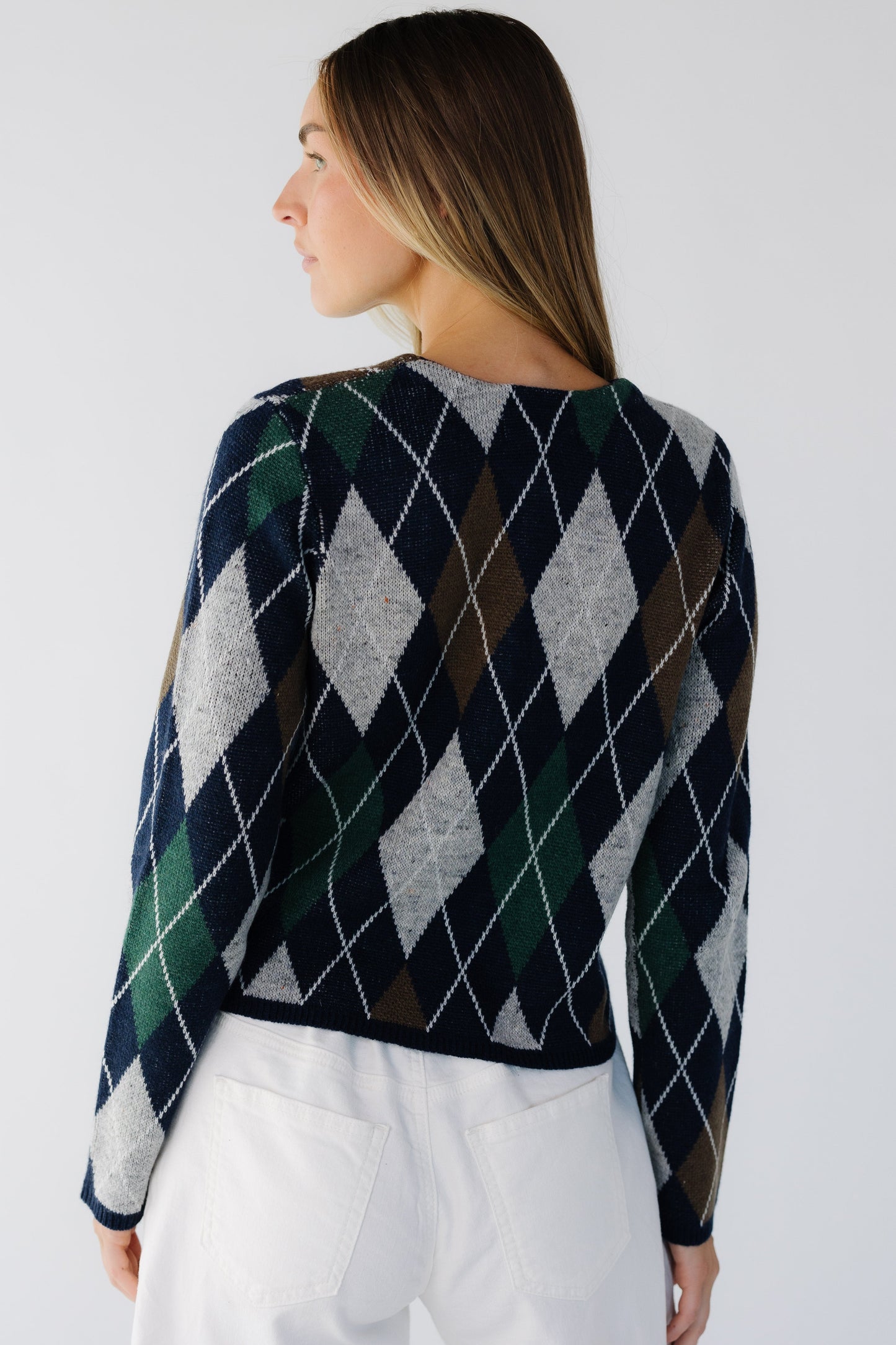 Back view of a woman wearing a navy, grey, brown & green argyle sweater with long sleeves.