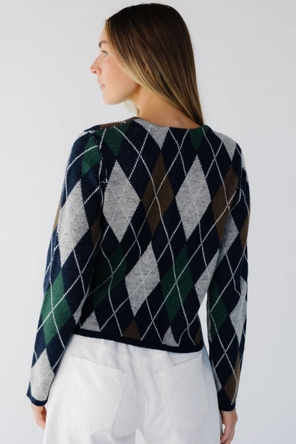 Back view of a woman wearing a navy, grey, brown & green argyle sweater with long sleeves.
