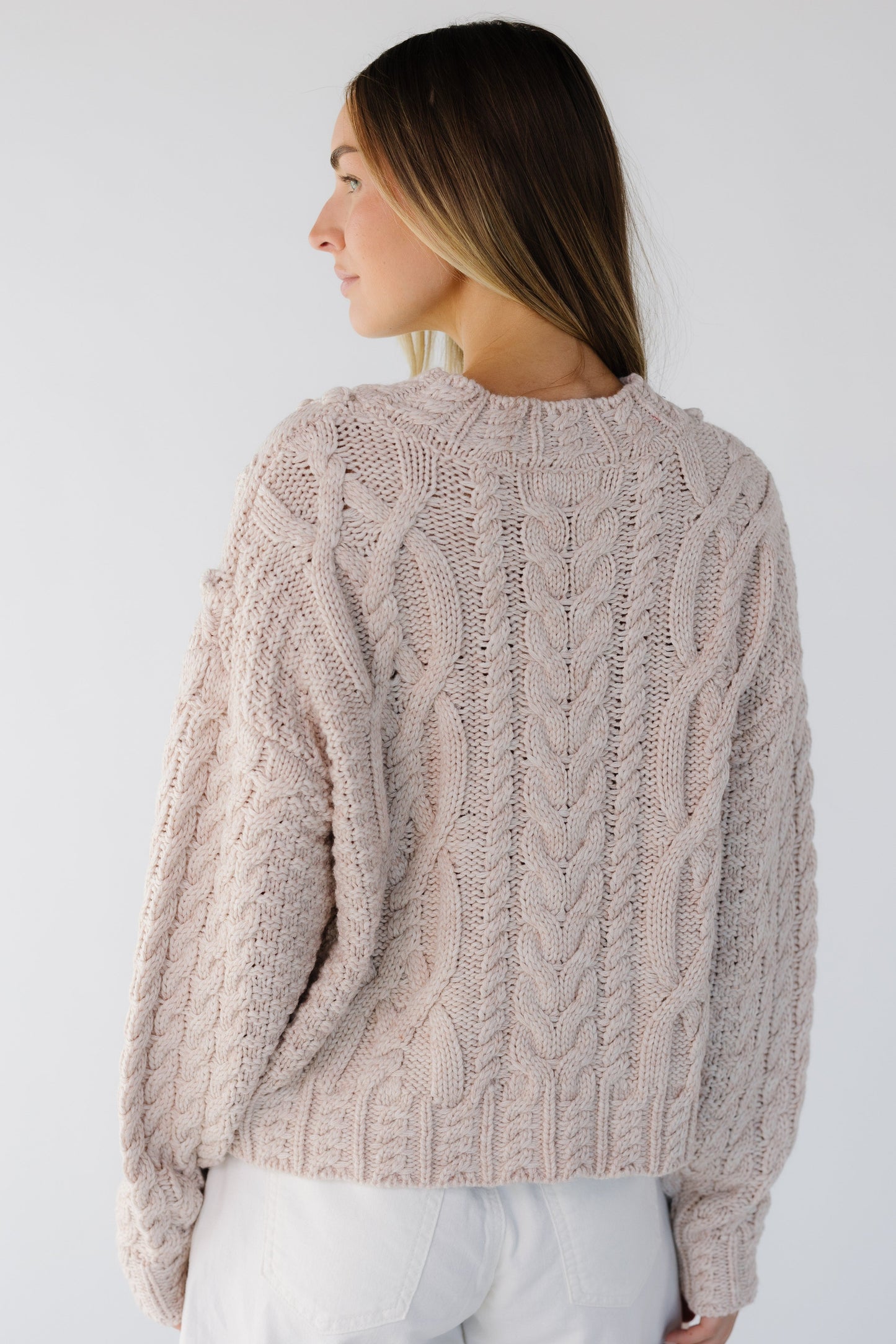 Back view of a woman wearing a loos ande cable knit sweater with drop shoulders and long sleeves.