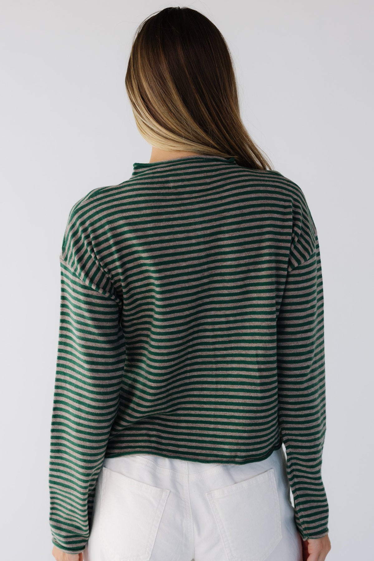 Back view of a woman wearing a loose fitting green & taupe stripe sweater with long sleeves.