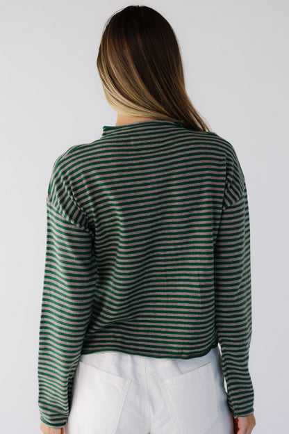 Back view of a woman wearing a loose fitting green & taupe stripe sweater with long sleeves.