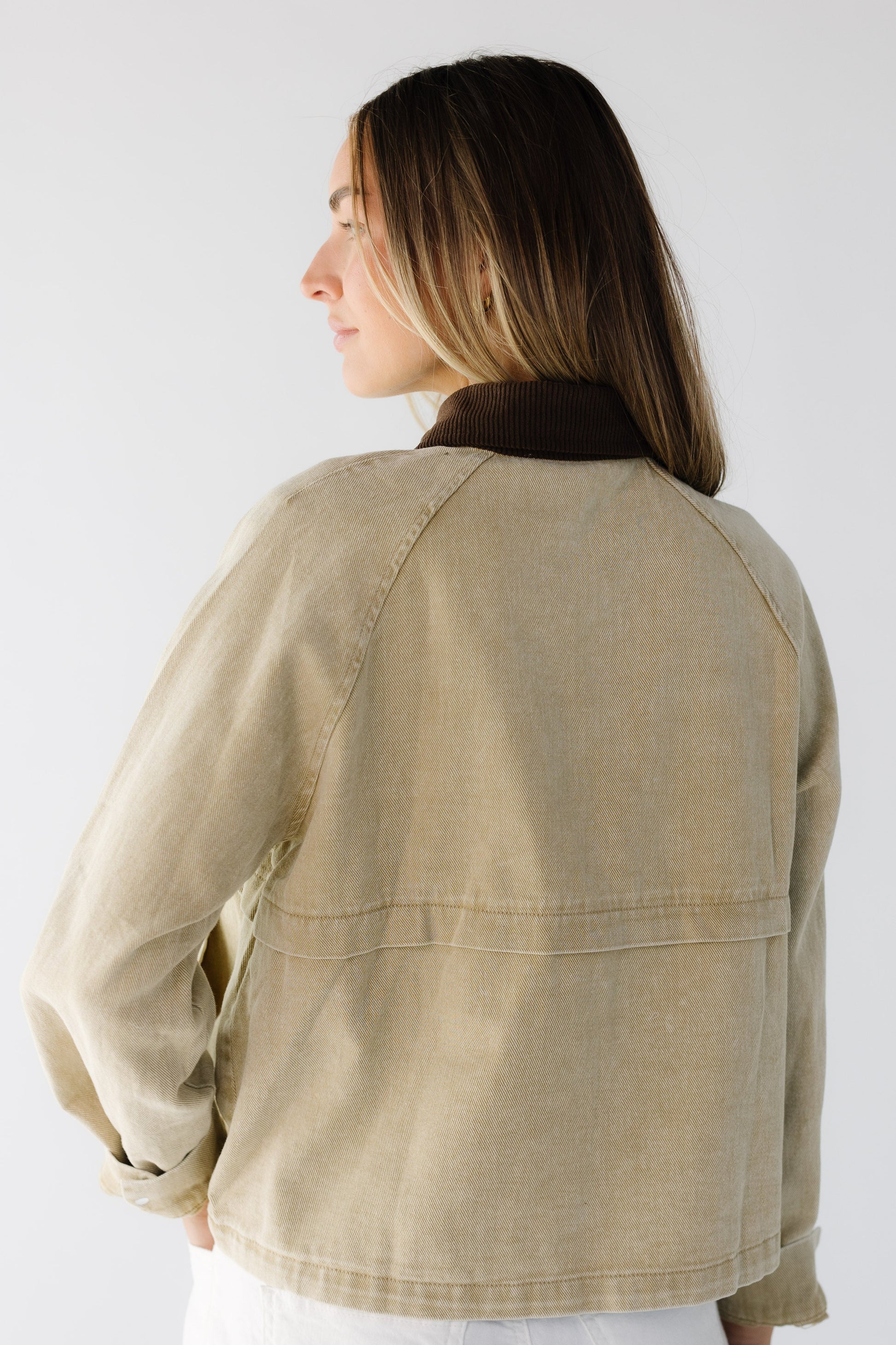 Back view of a dyoung woman wearing a tan loose fitting long sleeve jacket with decorative seam details and a brown corduroy collar.