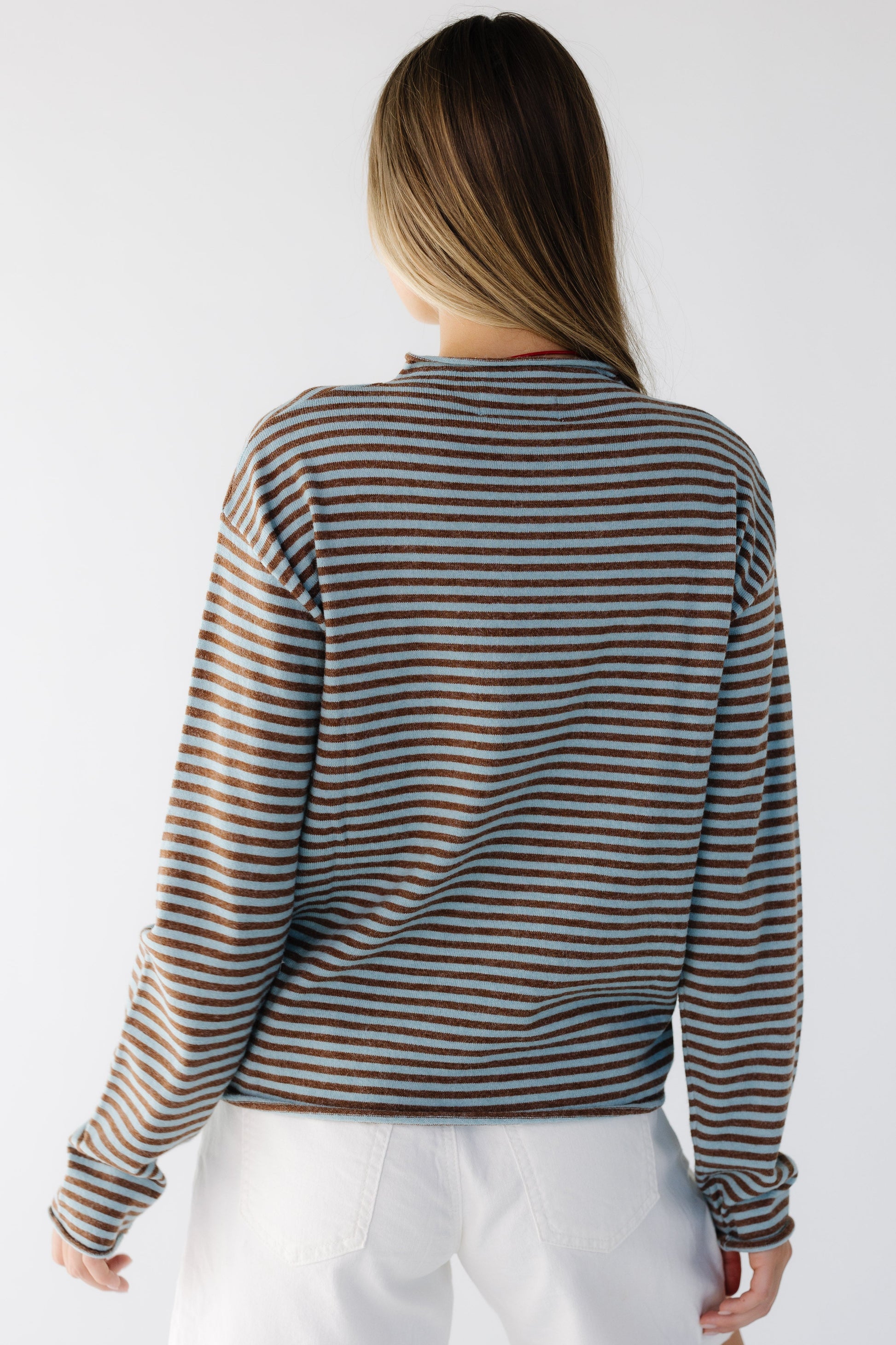 Back view of a woman wearing a teal & brown loose fitting stripe long sleeve top witn a mock turtleneck neckline.