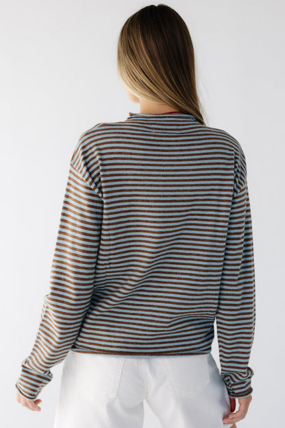 Back view of a woman wearing a teal & brown loose fitting stripe long sleeve top witn a mock turtleneck neckline.