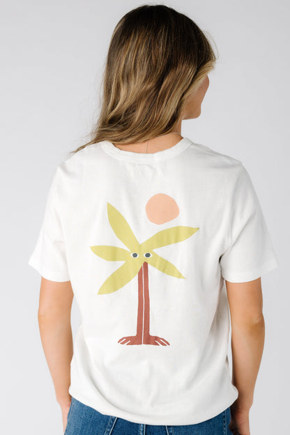 Back view of a woman wearing a white graphic tee with a large back graphic of  a palm tee and sun.