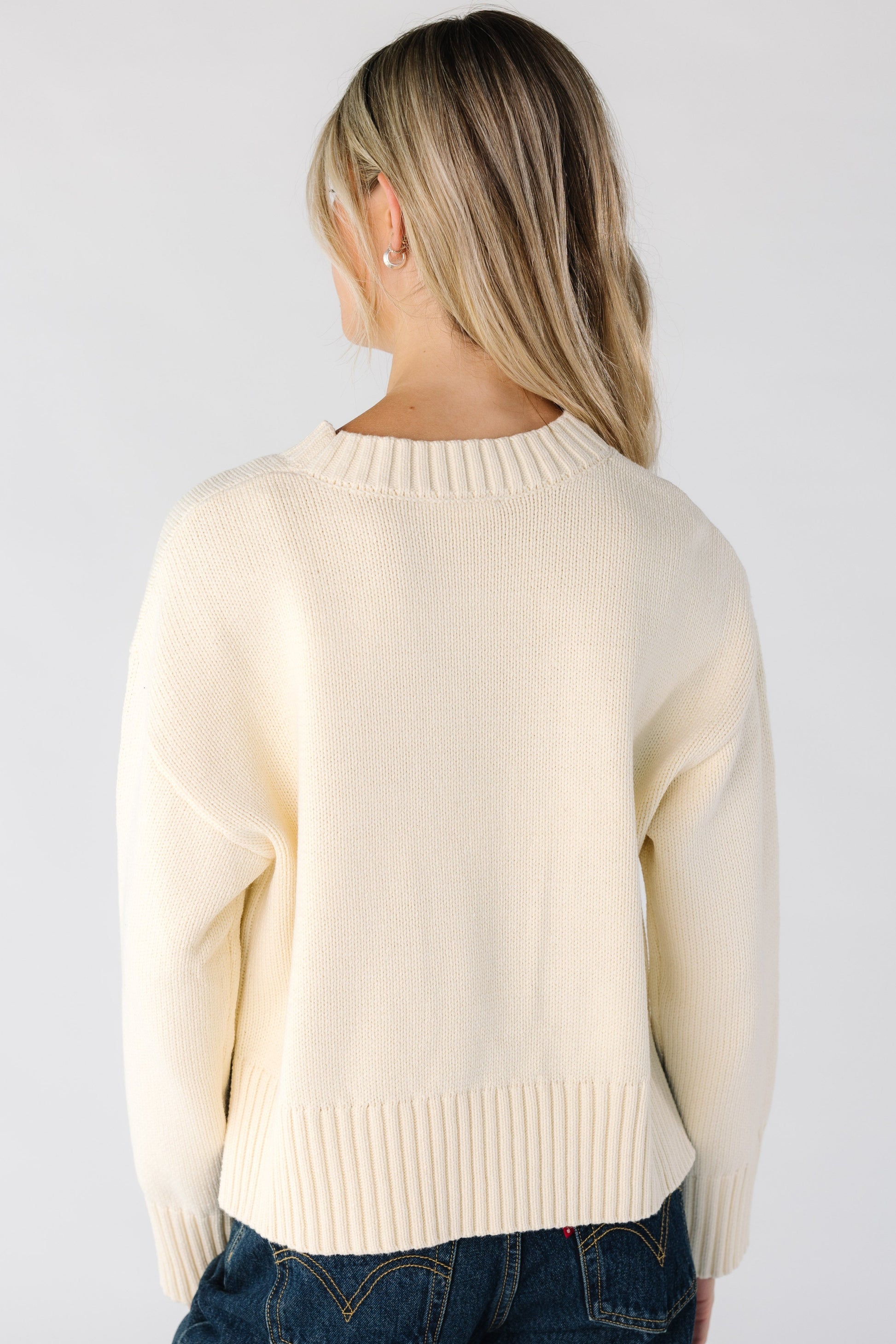 Back view of a woman wearing a loose fitting cream sweater with drop shoulder seams