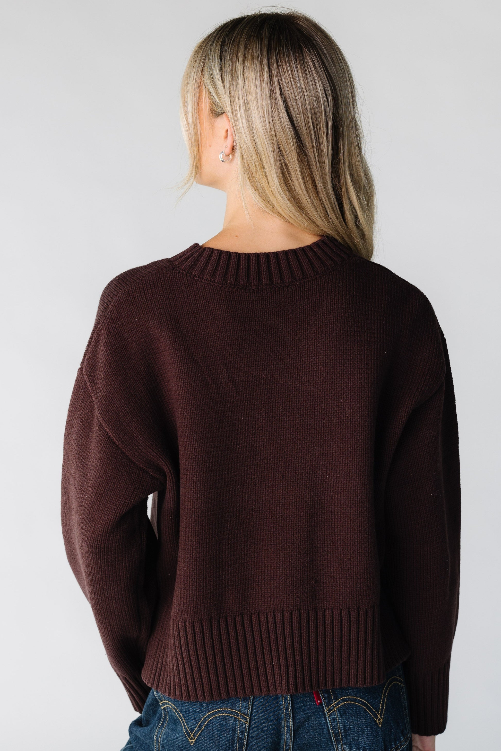 Back view of a woman wearing a brown loose fitting sweater with wide ribbing