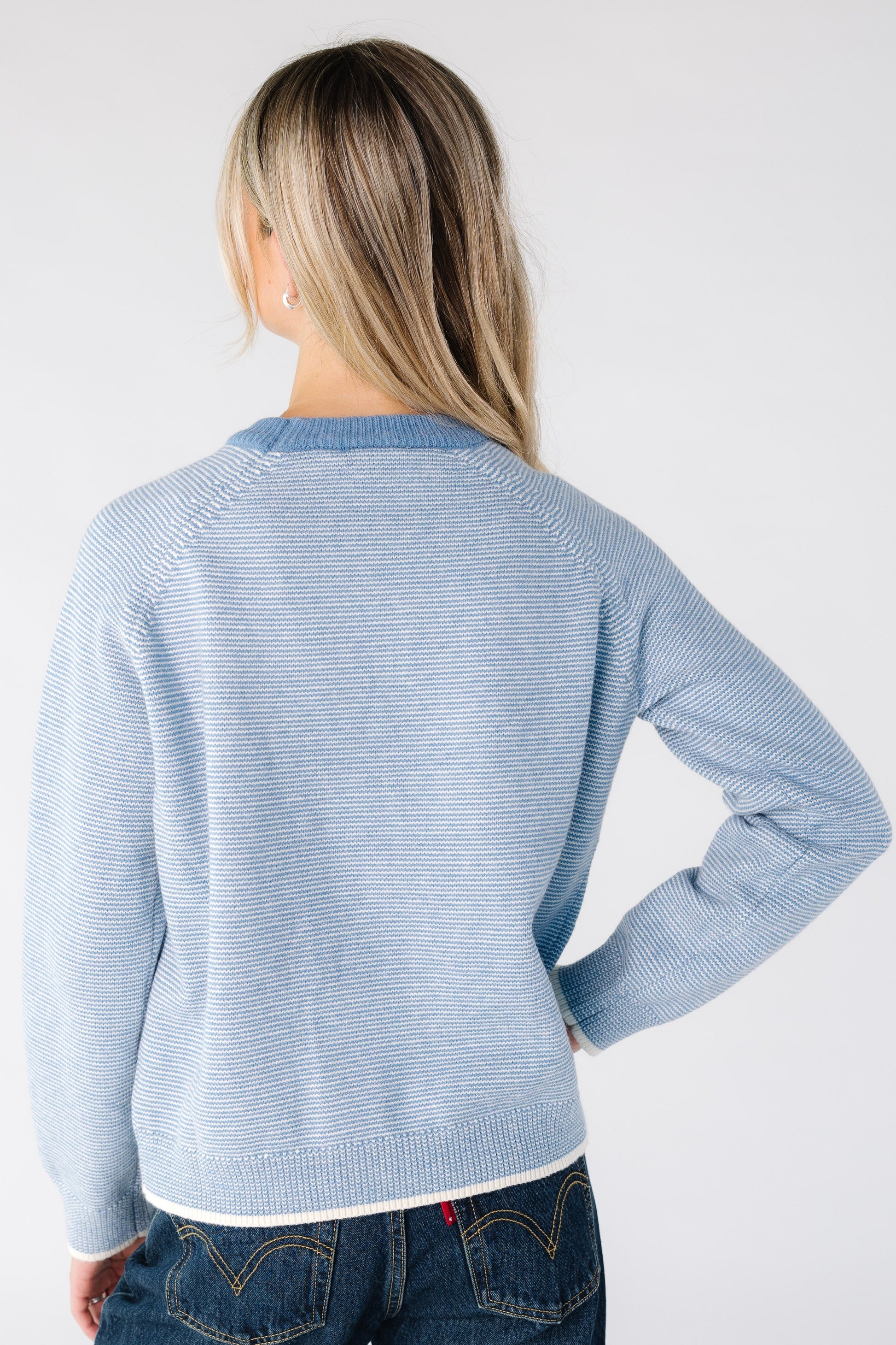 Back view of a woman wearing a blue and white narrow stripe sweater with long raglan sleeves