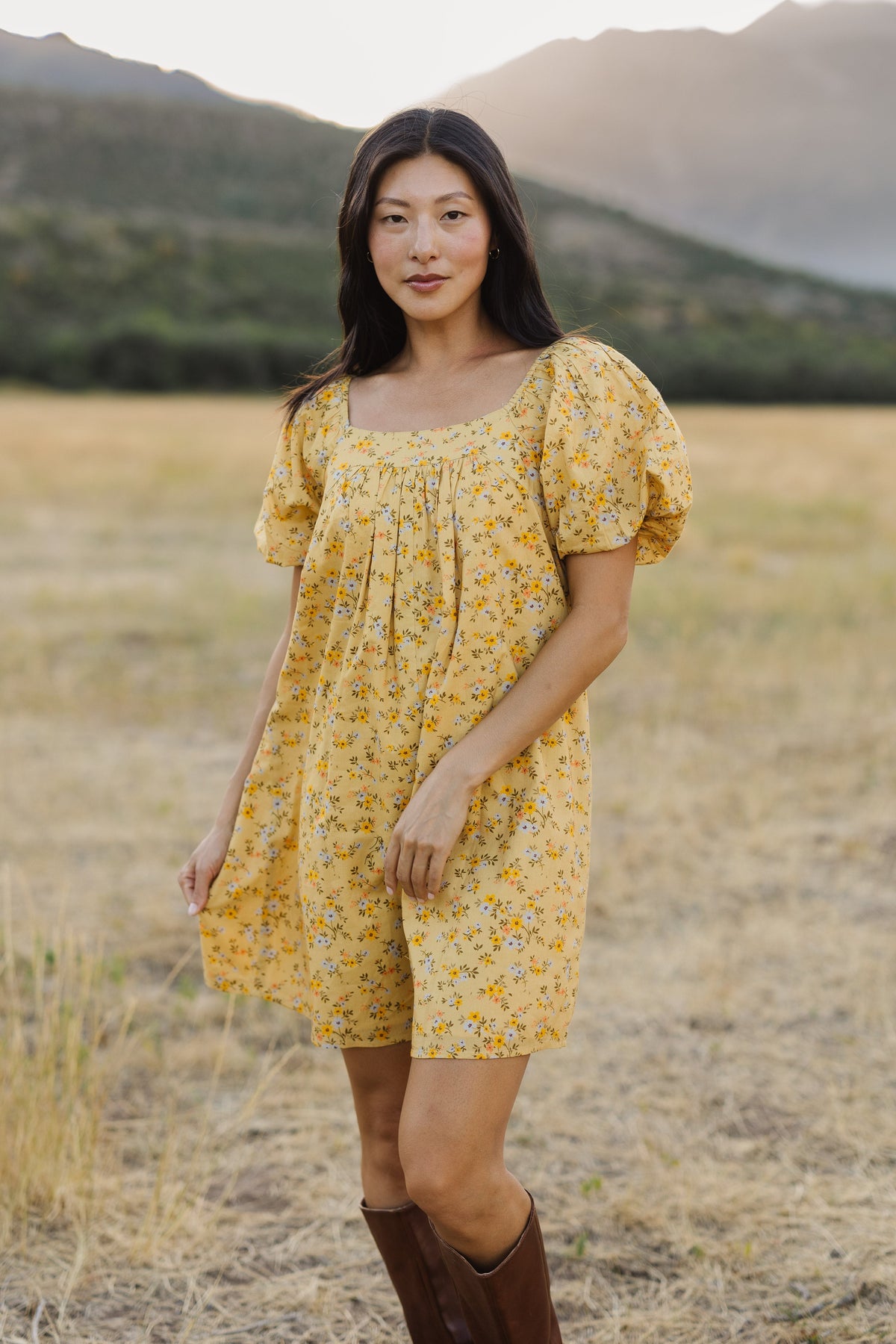 A young woman wearing a short yellow, floral print dress with a square neckline and balloon sleeves.