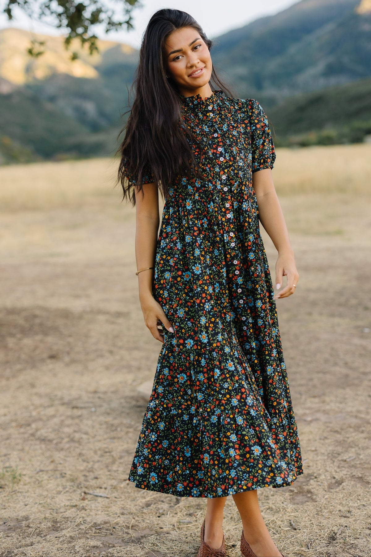 Woman wearing a black and floral pirnt midi-maxi dress with short sleeves and a ruffle collar.