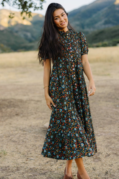 Woman wearing a black and floral pirnt midi-maxi dress with short sleeves and a ruffle collar.