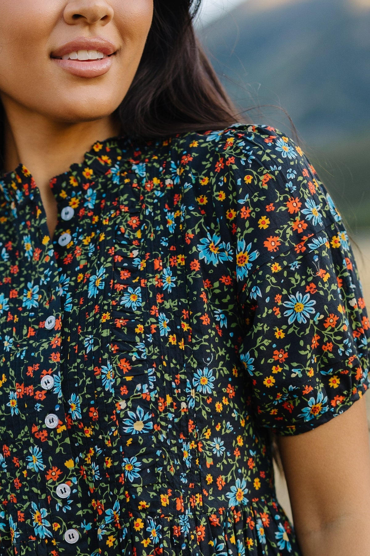 Close up view of a woman wearing a black floral button down dress with short puff sleeves.