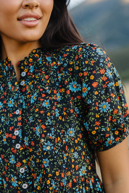 Close up view of a woman wearing a black floral button down dress with short puff sleeves.