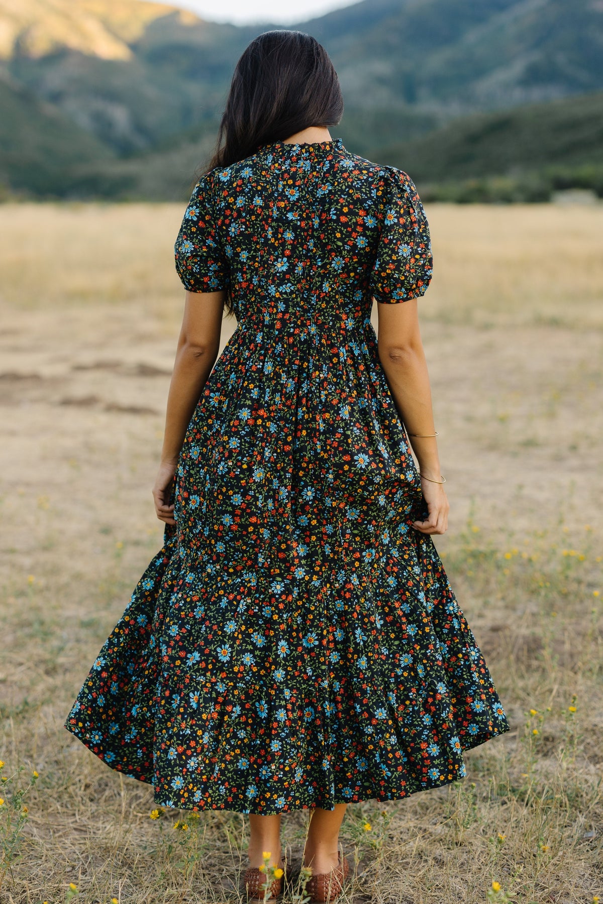 Back view of a woman wearing a slightly loose fitting midi-maxi dress with puff sleeves.