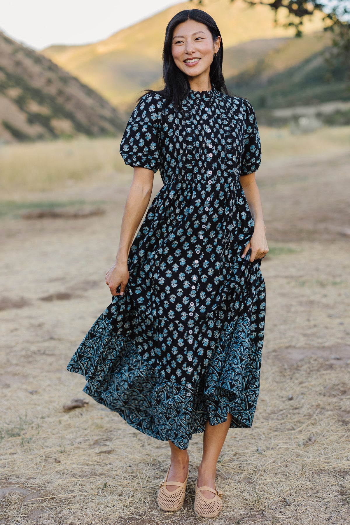 Young woman wearing a modest navy & blue floral button down dress with puff sleeves and a wide bottom ruffle in a different print.