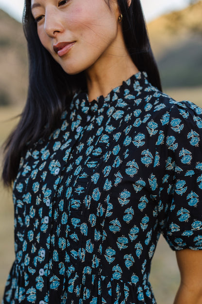 Close up view of a woman wearing a navy floral button down dress with shot puf sleeves and a ruffled neckline.