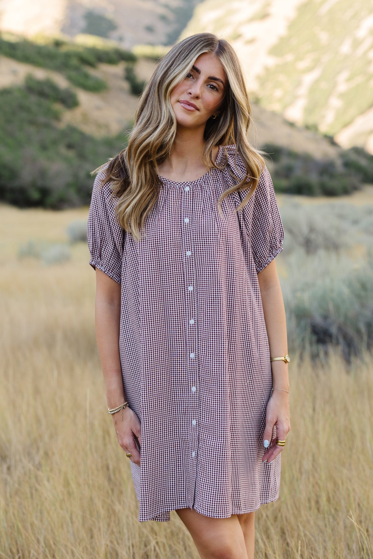Young woman wearing a modest button down dress in  burgundy & white gingham with a round neckline and short sleeves.