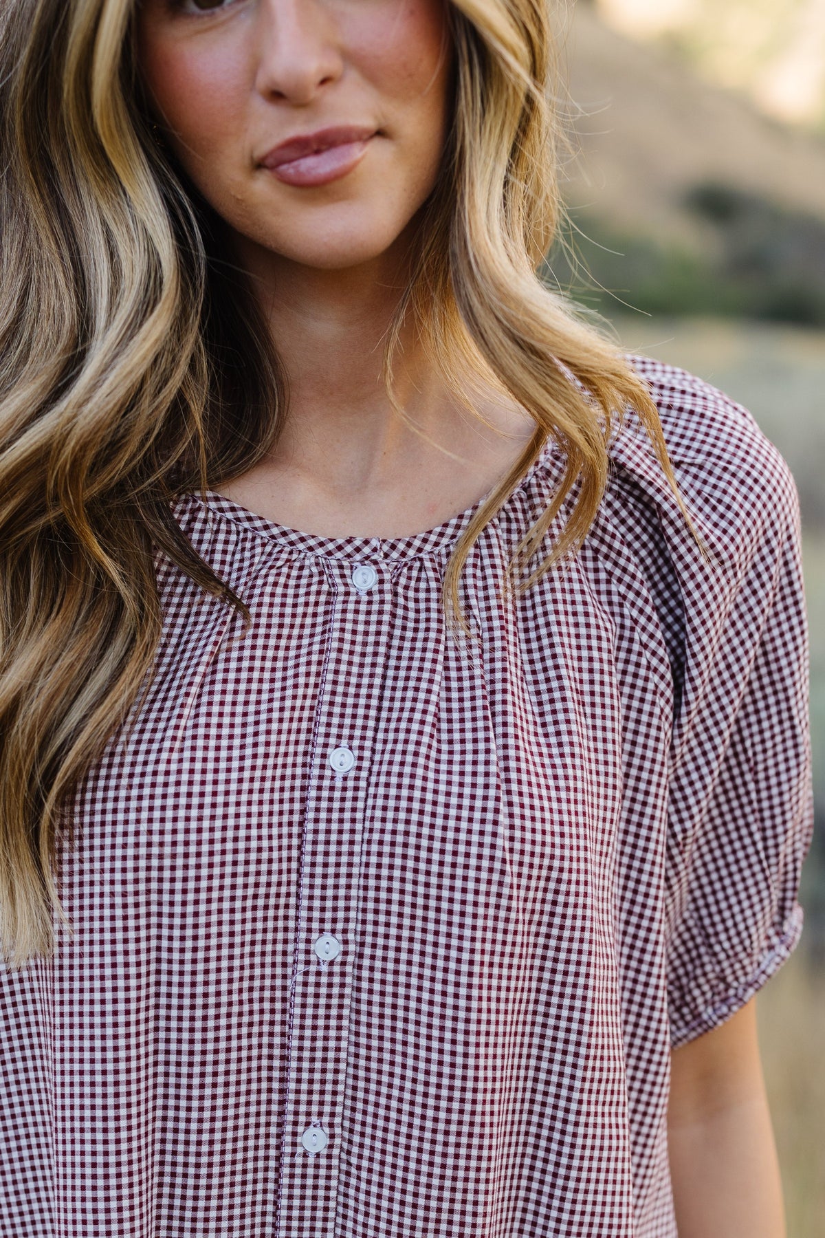 Close view of a woman wearing a burgundy, button down dress with short puff sleeves and a round neckline.