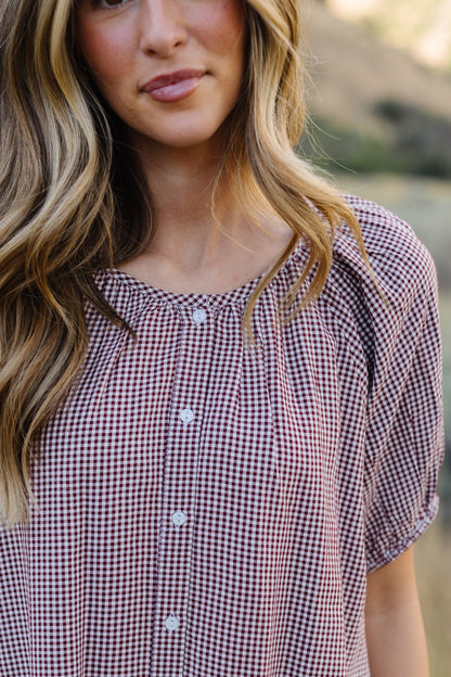 Close view of a woman wearing a burgundy, button down dress with short puff sleeves and a round neckline.