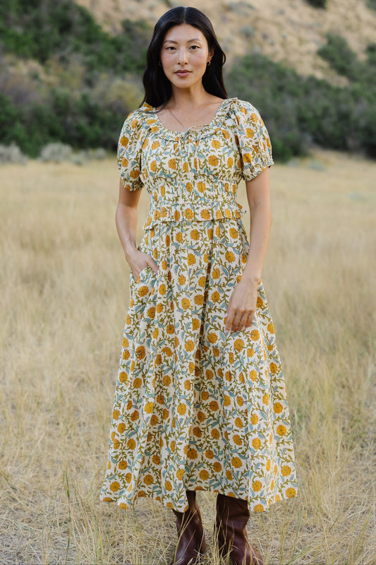 Young woman wearing a modest floral print midi dress with a ruffled scoop neckline, puff sleeves,wide waistband and a full skirt.
