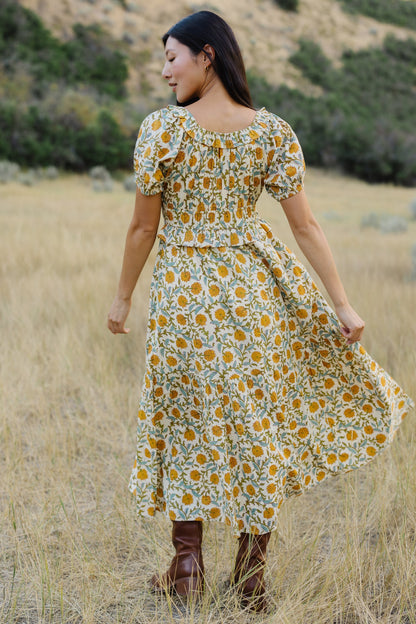 Back view of a woman wearing a yellow floral midi dress with short puff sleeves, and full skirt.