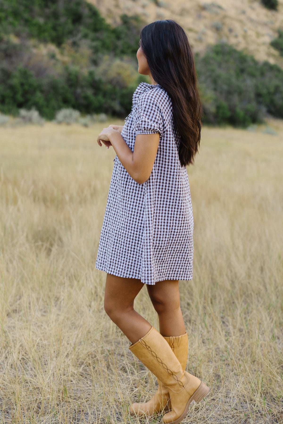 Side view of a woman wearing a brown & white gingham dress with puff sleeves.