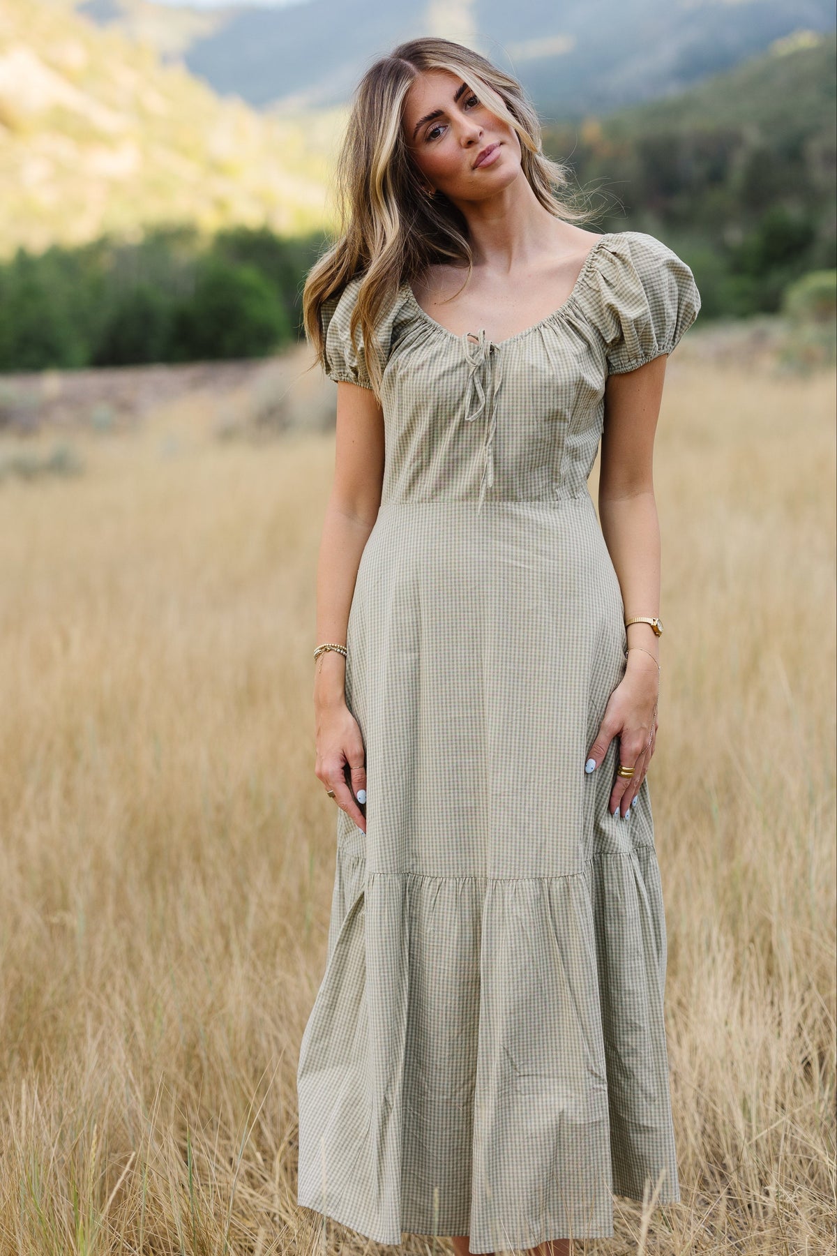 Young woman wearing a modest light green gingham midi dress with a scoop neckline and short puff sleeves.