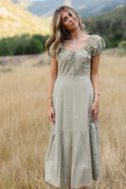 Young woman wearing a modest light green gingham midi dress with a scoop neckline and short puff sleeves.