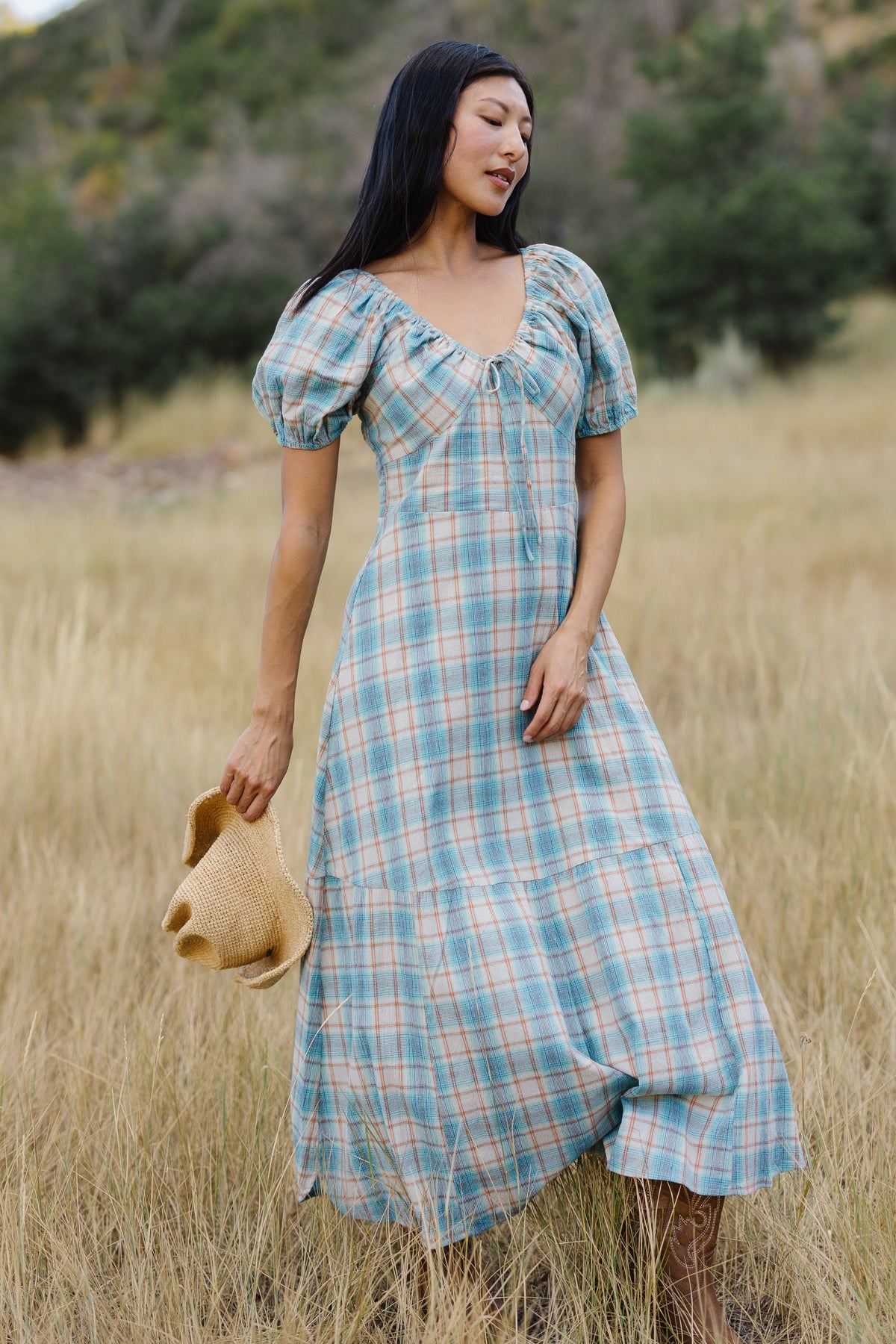 Young woman wearing a modest blue plaid midi dress with a scoop drawstring neckline, puff sleeves and an empire waist.