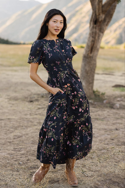 Young woman wearing a modest navy floral midi dress with a V-neckline, short sleeves, wide elastic waistband and side pockets.