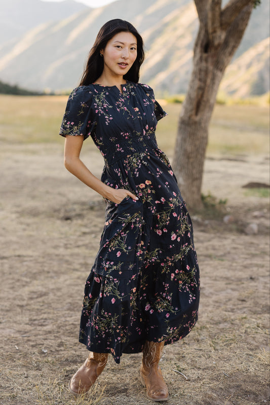 Young woman wearing a modest navy floral midi dress with a V-neckline, short sleeves, wide elastic waistband and side pockets.