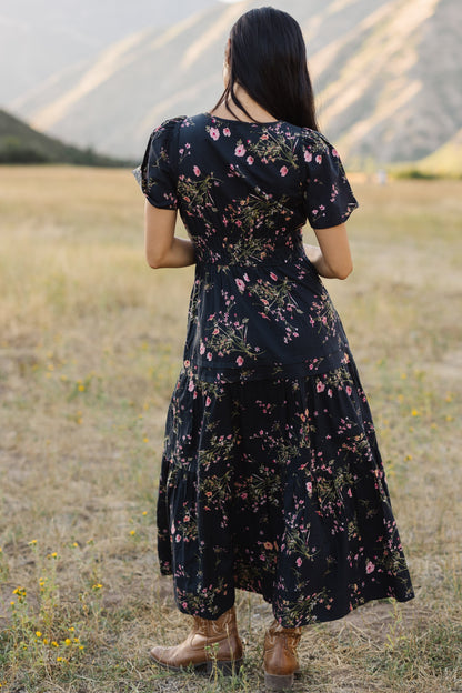 Back view of a woman wearing a navy floral print midi dress with shrot sleeves,wide elastic waist and full skirt.