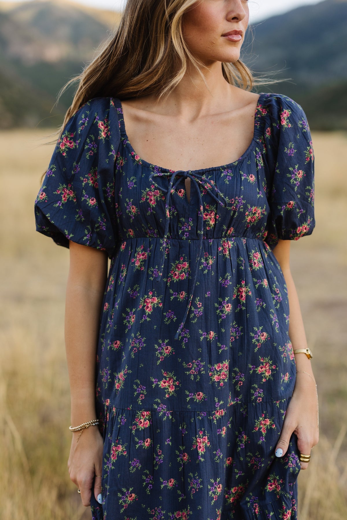 Close up view of a young woman wearing a navy floral dress with a drawstring scoop neckline and large puff sleeves and empire waist.