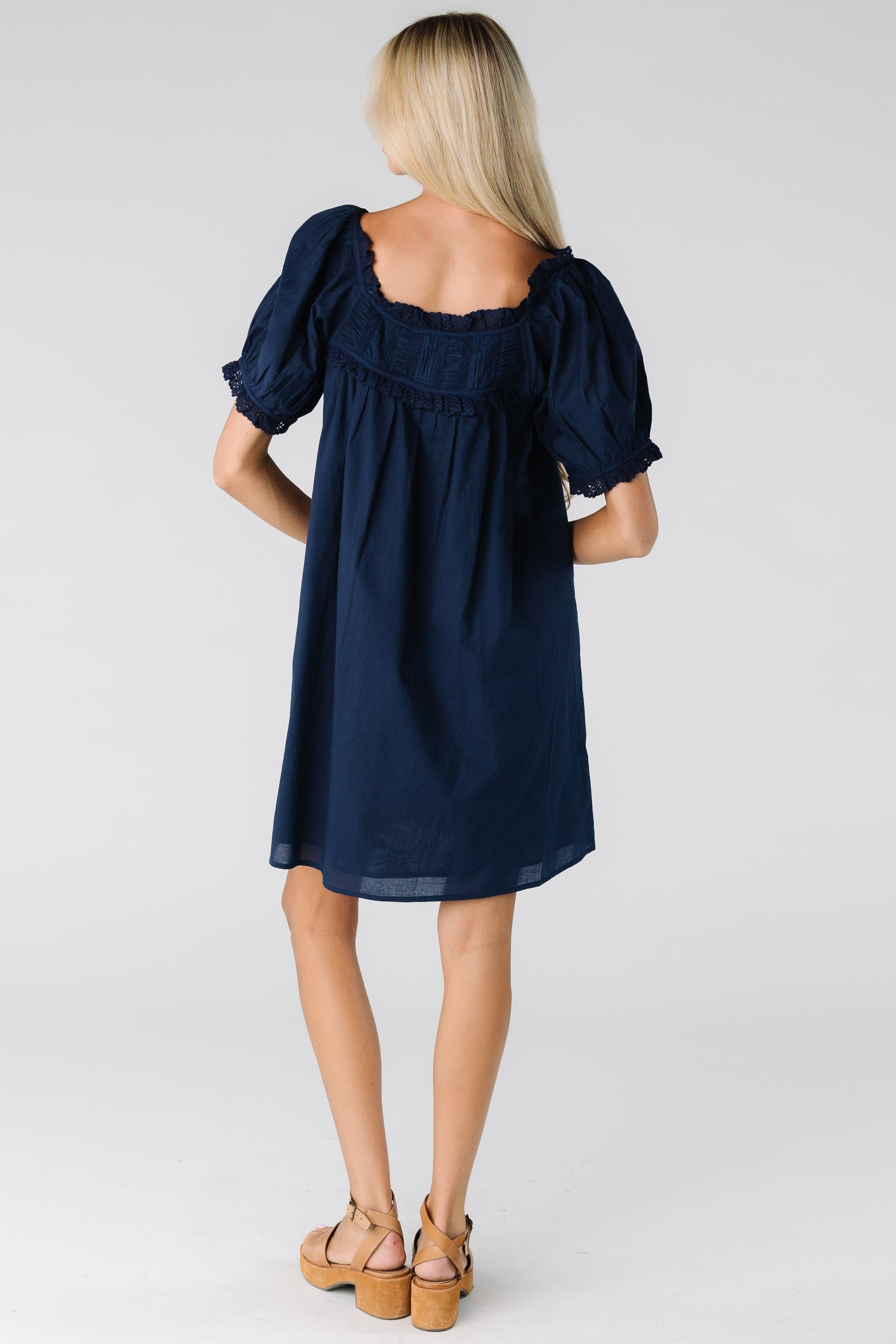 Back view of a woman wearing a navy dress with square back neckline and short sleeves with lace cuffs
