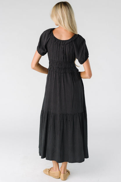 Back view of a woman wearing a black polka dot midi dress with a wide bottom ruffle, short balloon sleeves and a wide waist and scoop neckline.
