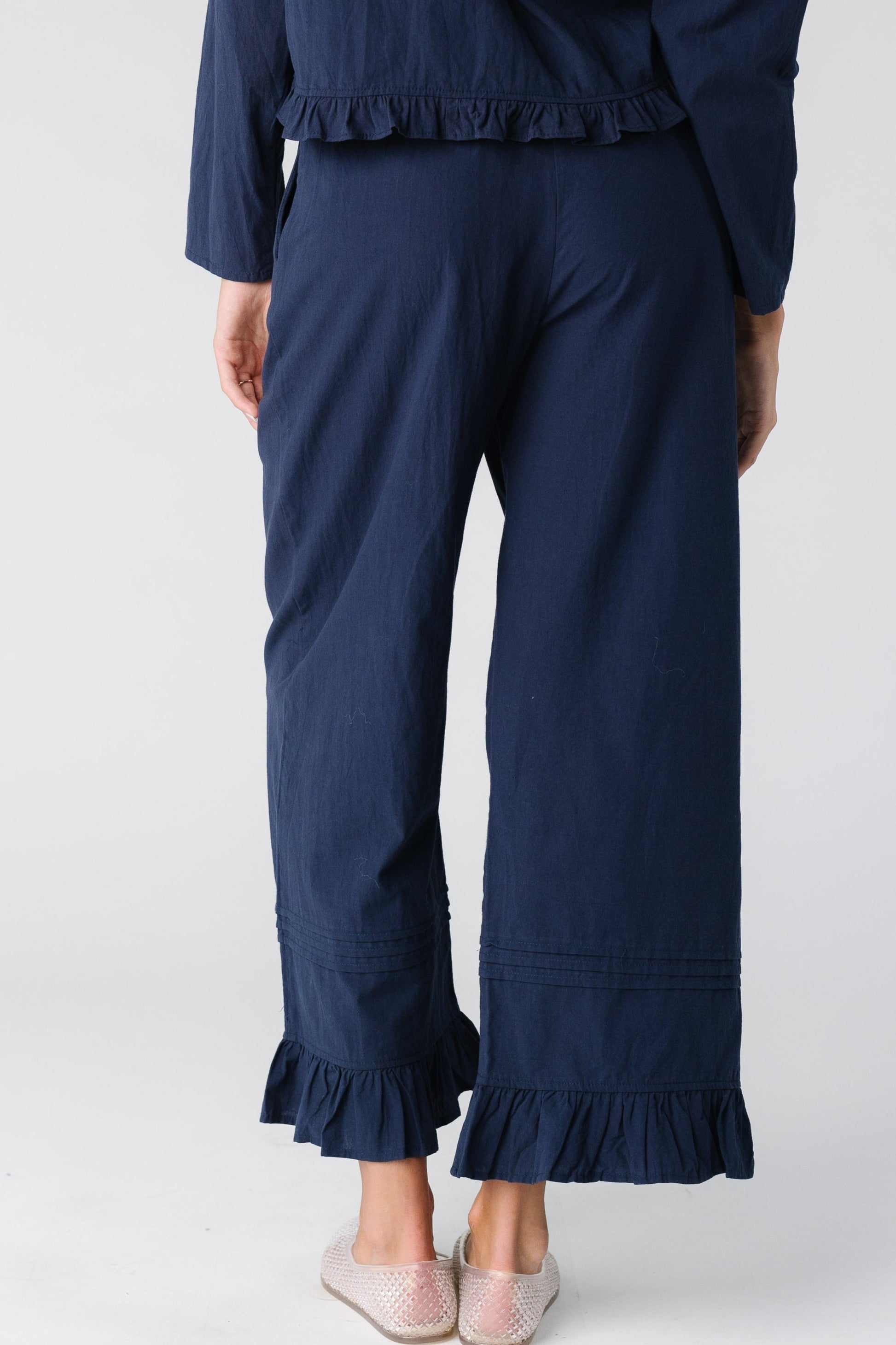 Back view of a woman wearing a pair of navy wide leg trousers with ruffle hem