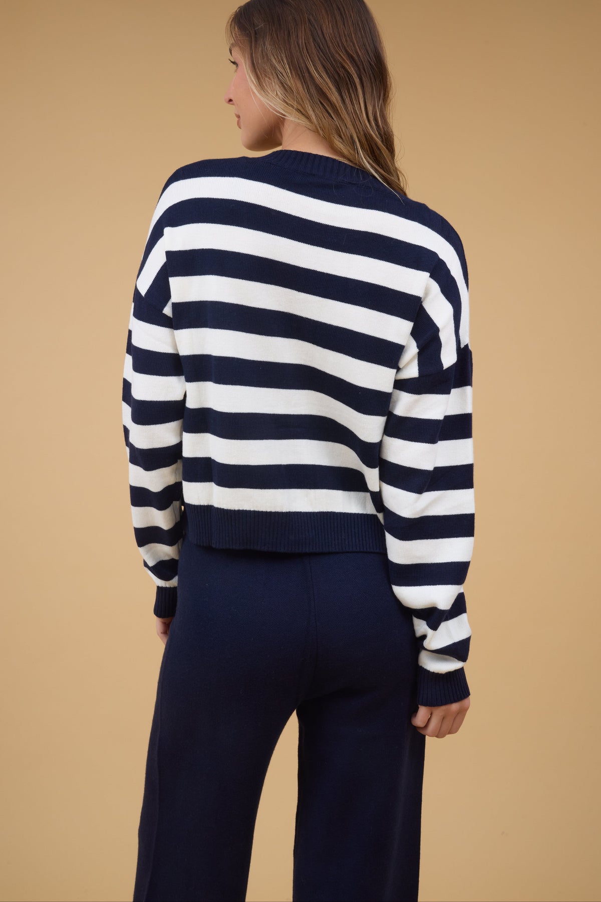 Back view of a woman wearing a 2 piece set with navy & white stripe cardigan with long sleeves and wide leg navy sweater pants.