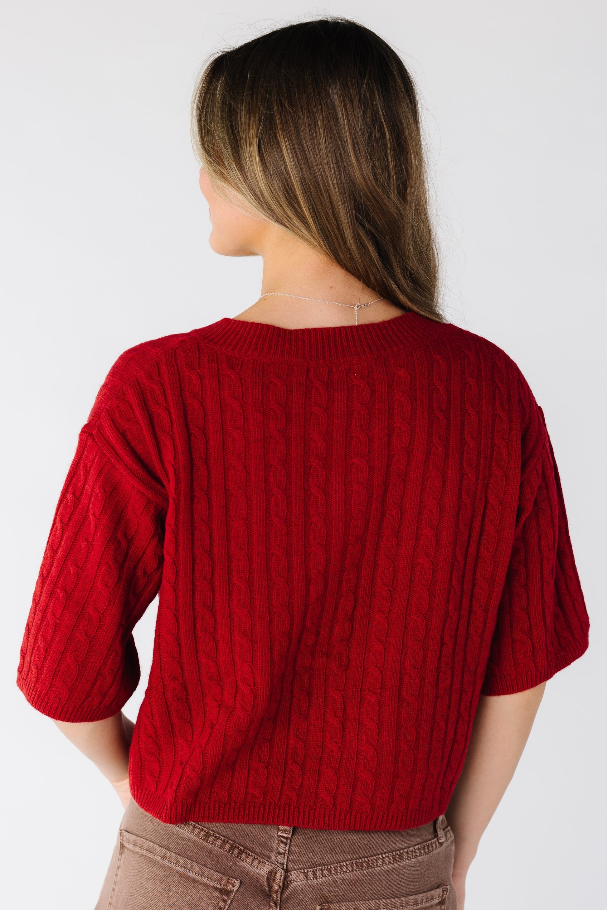Back view of a woman wearing a red cable knit cardigan with short sleeves