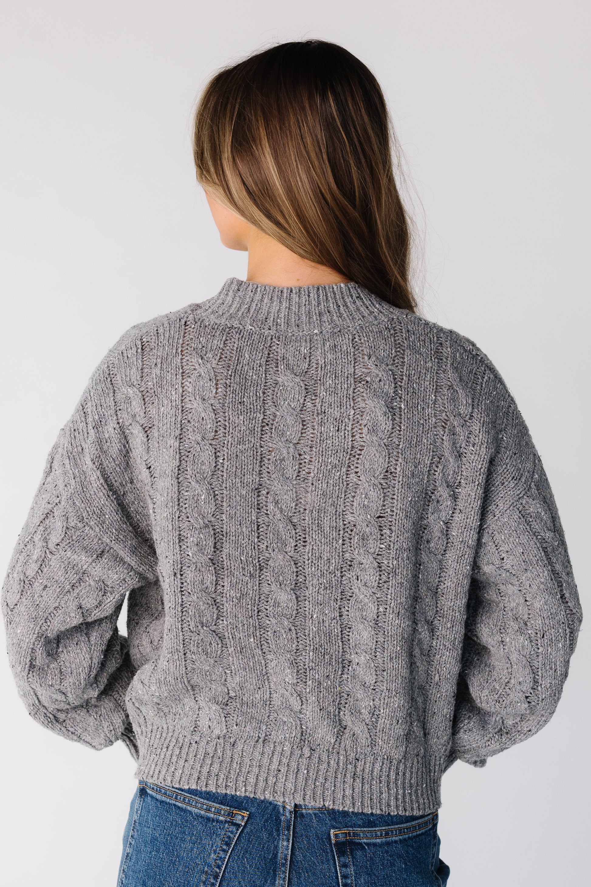 Back view of a woman wearing a grey cable knit sweater