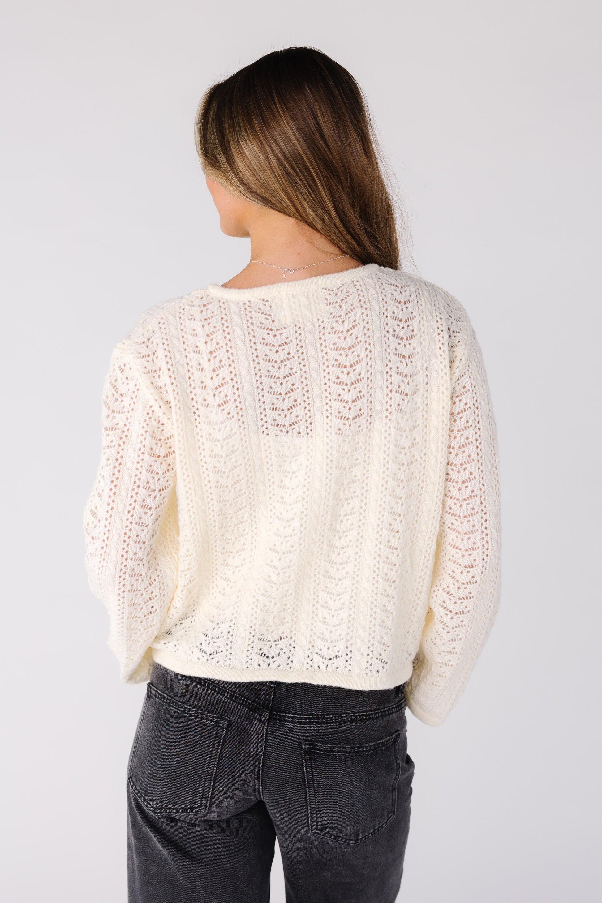 Back view of a woman wearing a cream lace cardigan 