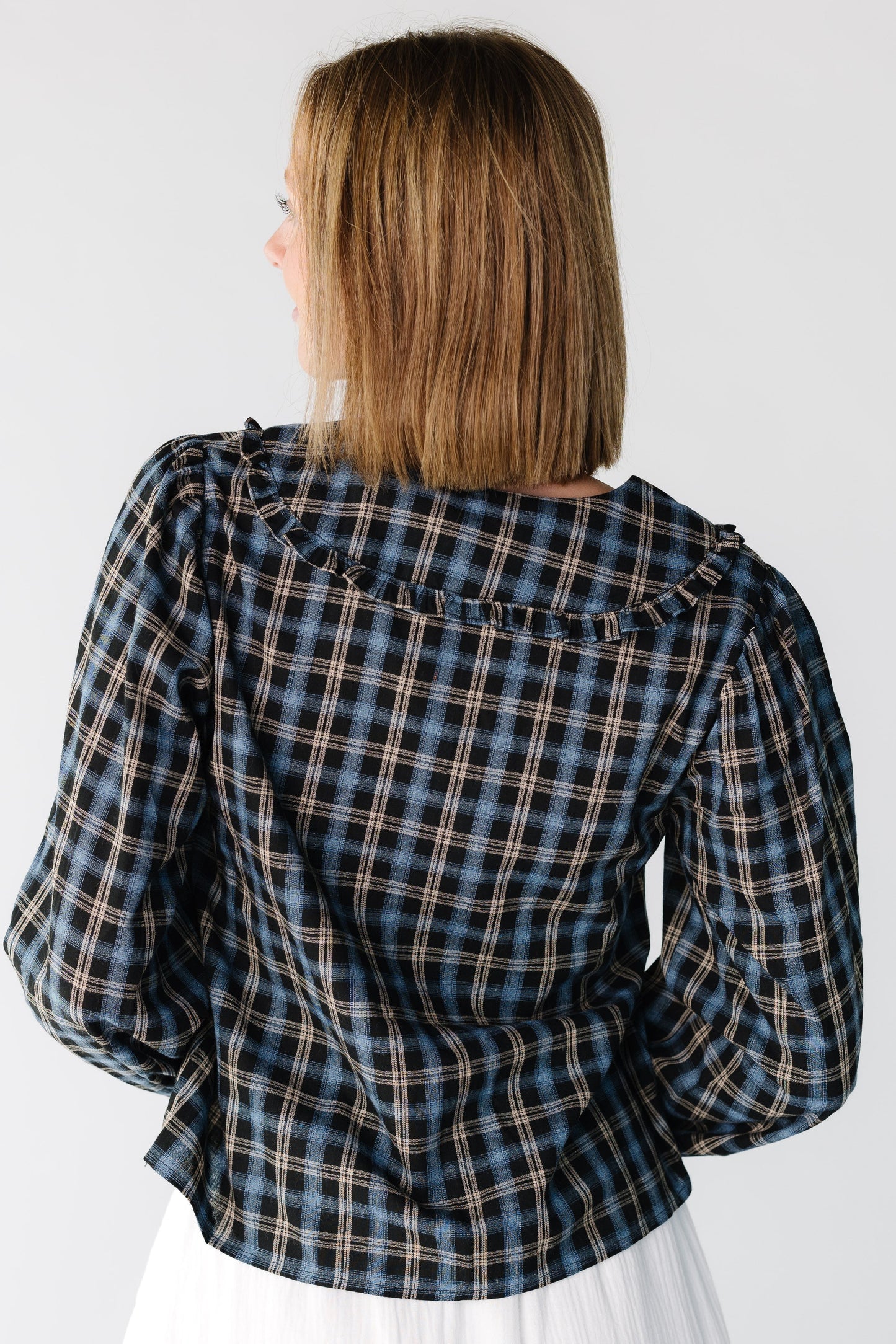 Back view of a woman wearing a navy plaid long sleeve top with a ruffled collar