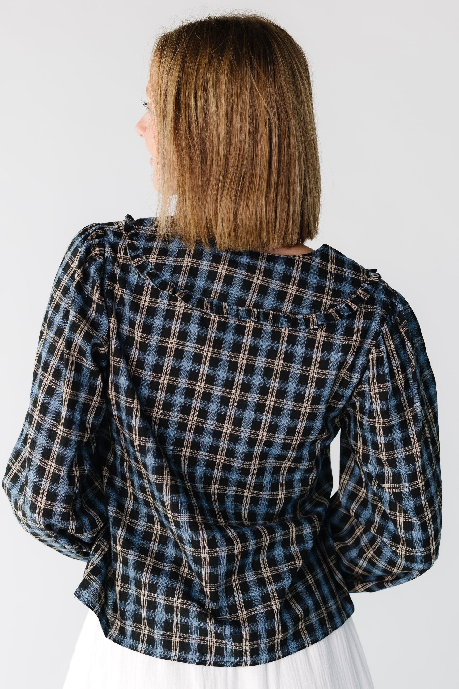 Back view of a woman wearing a navy plaid long sleeve top with a ruffled collar