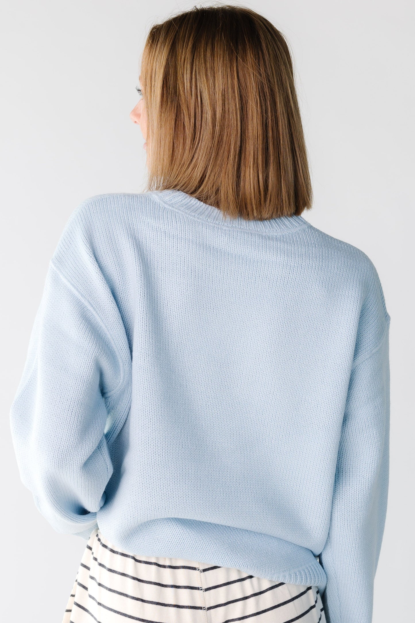 Back view of a woman wearing a light blue sweater with long sleeves
