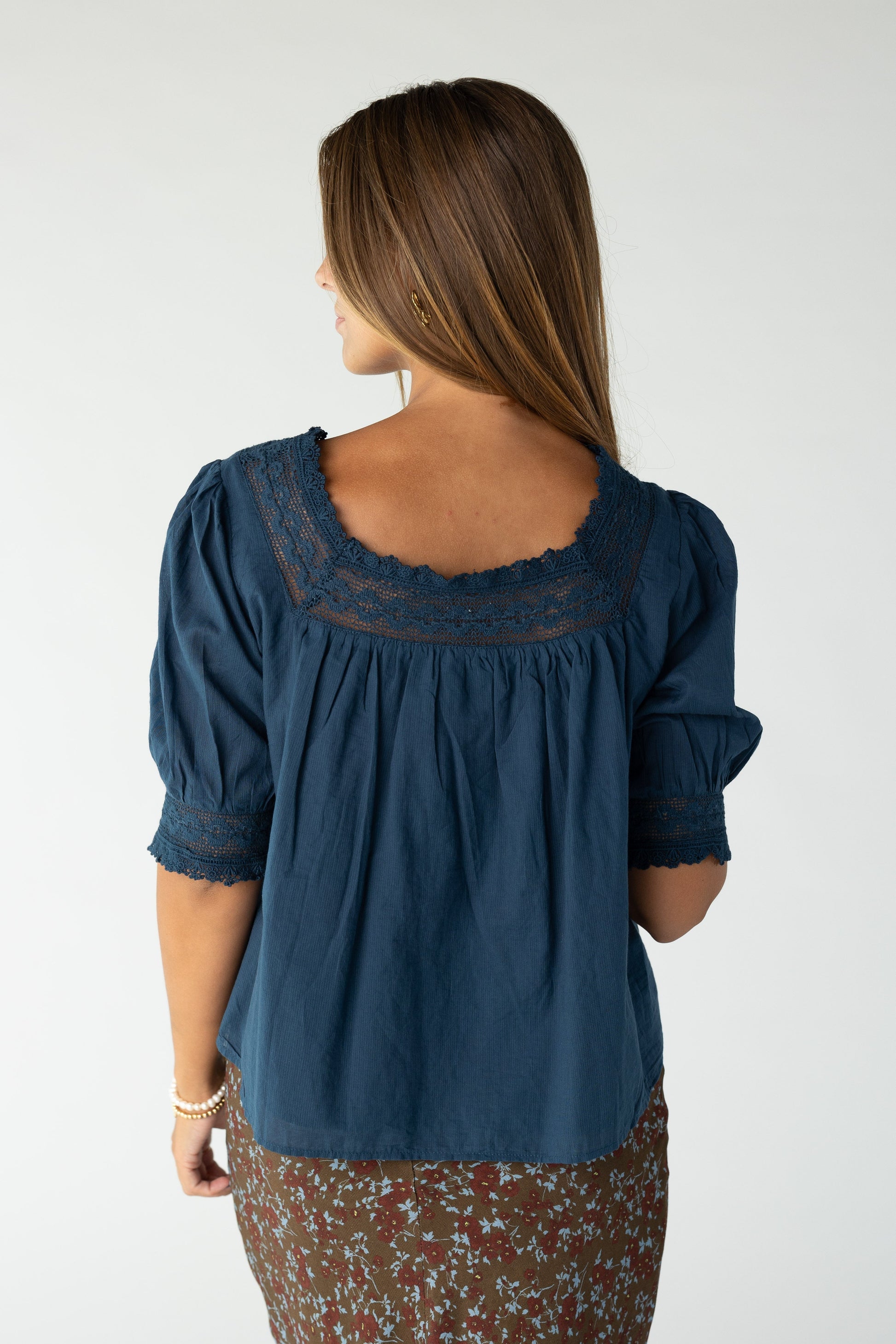 Back view of a woman wearing a navy blouse with square lace neckline