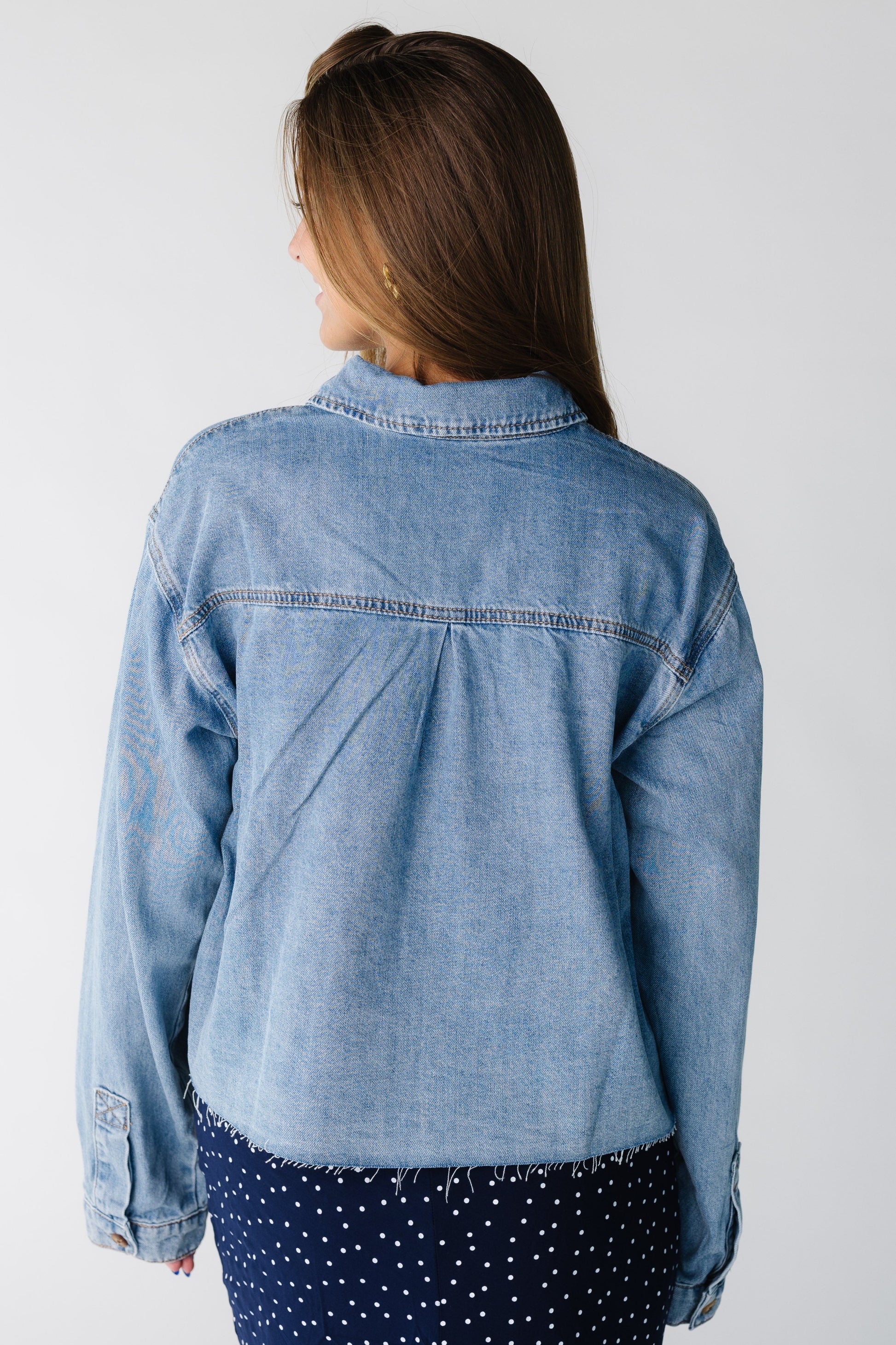 Back view of a woman wearing a loose denim shirt with fraying hem