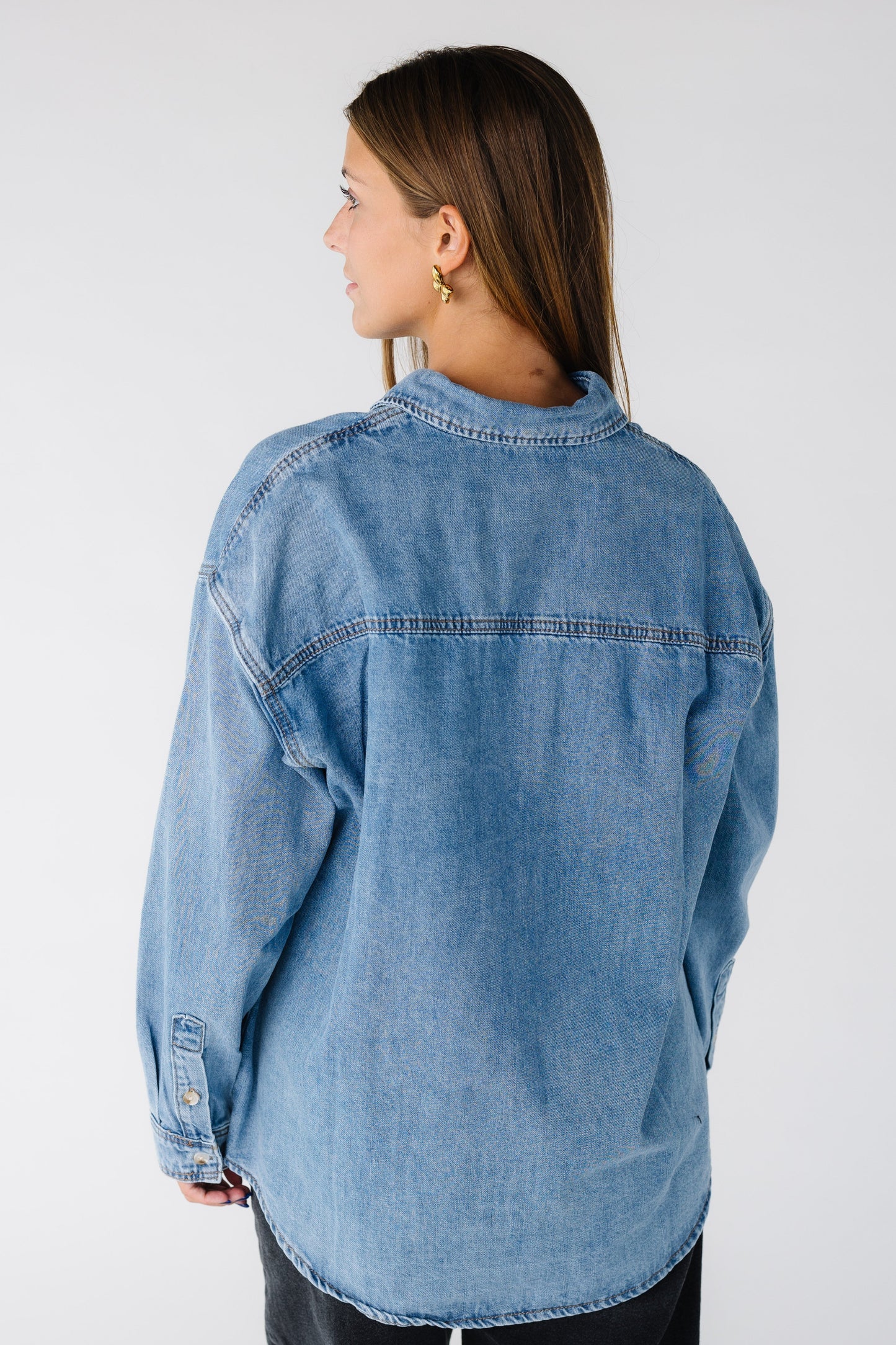 Back view of a woman wearing a loose fitting medium denim shirt