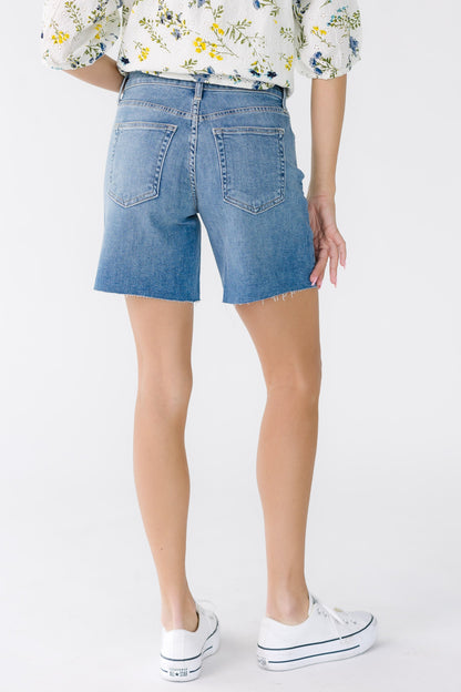 Back view of a woman wearing a  pair of medium denim shorts with 2 back pockets and scissor cut hems.
