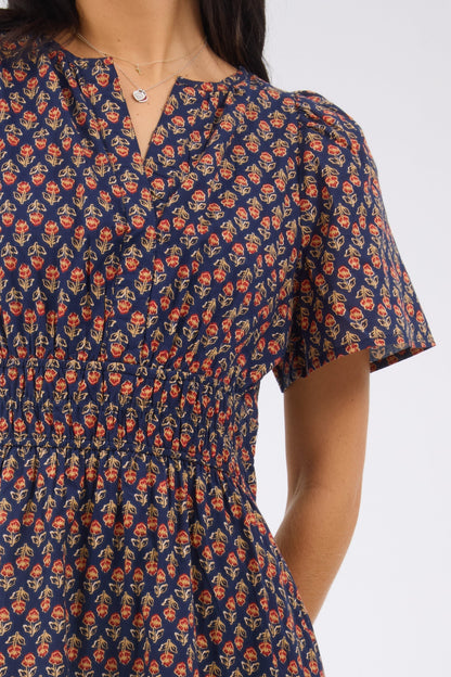 Close up view of a navy floral dress with a v-neckline, short sleeves and a wide elastic waistband.