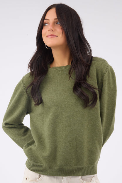 A woman wearing an olive crew neck sweater with long sleeves.